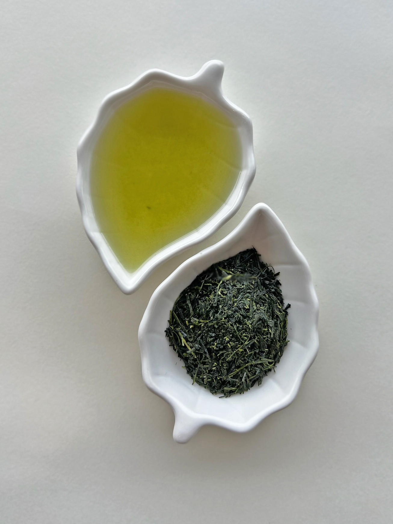 "Close-up photograph of Gyokuro green tea leaves and steeped tea, showing vibrant, deep green color and delicate, glossy texture, neatly arranged on a white ceramic leaf plate."