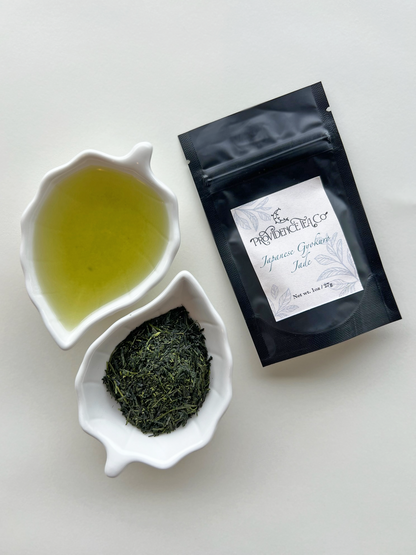 "Close-up photograph of Gyokuro green tea leaves and steeped tea, showing vibrant, deep green color and delicate, glossy texture, neatly arranged on a white ceramic leaf plate, next to a bag of packaged tea